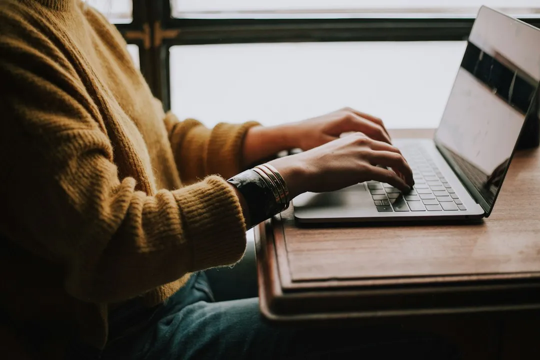 Personne assise à un bureau qui tape un message sur un ordinateur portable, les deux mains sur le clavier