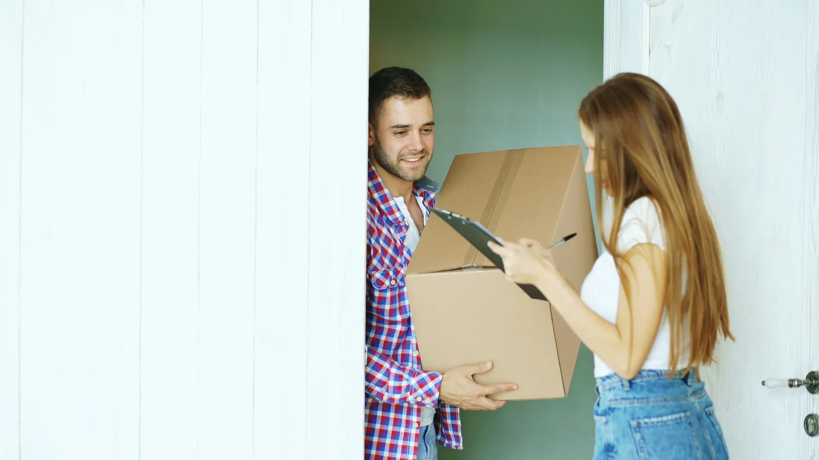 Livreur remettant un colis en carton à une cliente qui signe le bon de livraison sur le pas de sa porte