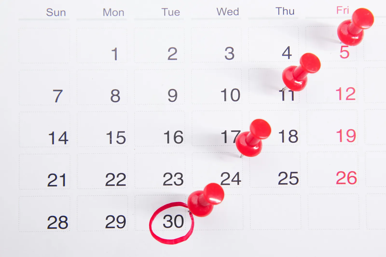 Calendrier mural blanc avec des punaises rouges plantées sur plusieurs dates, pour marquer des échéances