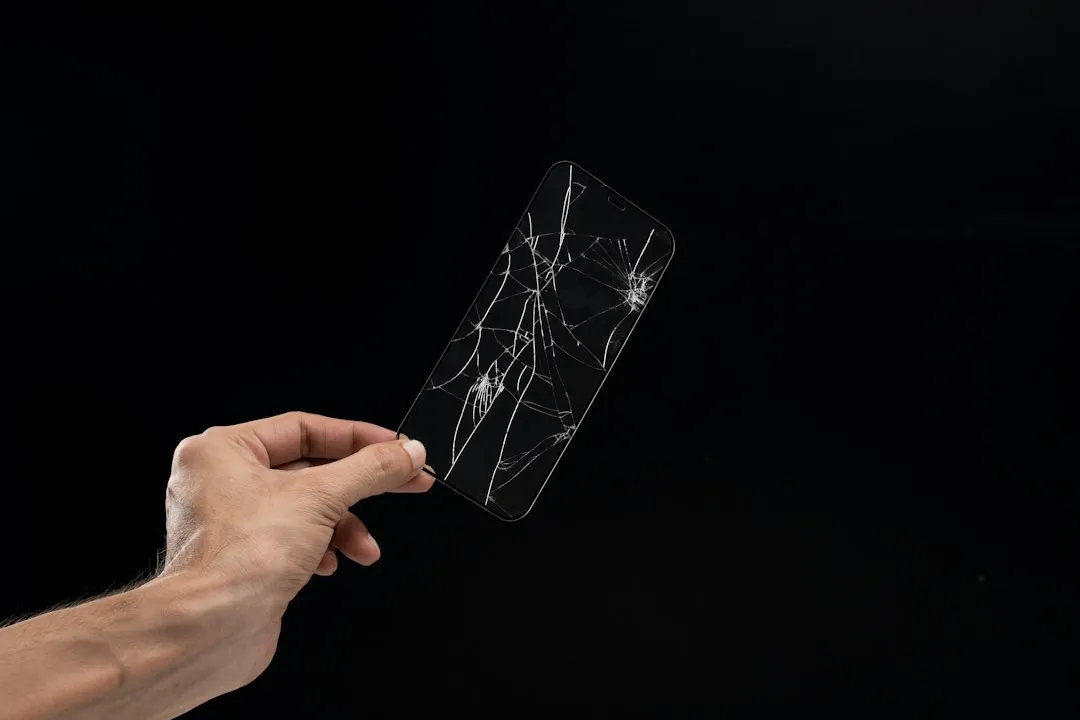 Main qui tient un smartphone à l'écran fissuré, sur fond sombre