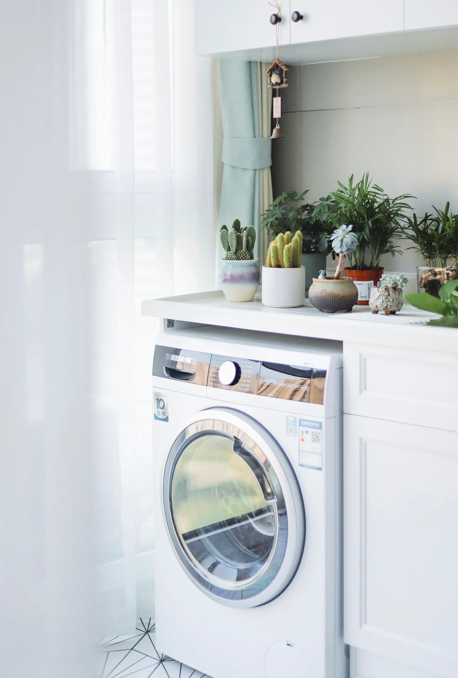 Lave-linge blanc à hublot sous un plan de travail, avec des plantes posées au-dessus