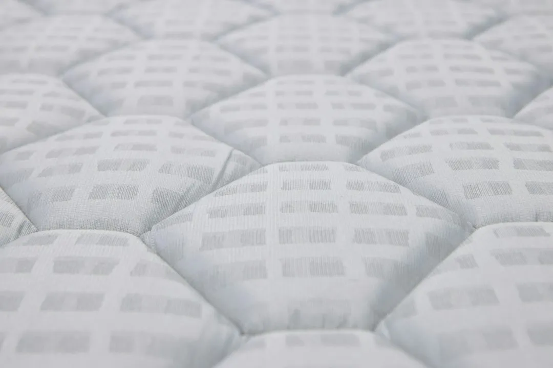Gros plan sur la surface blanche matelassée d'un matelas, avec ses coutures et son relief capitonné