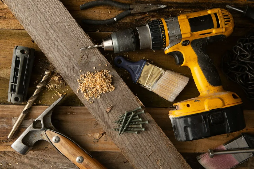 Perceuse sans fil, marteau et autres outils posés sur une table en planches de bois