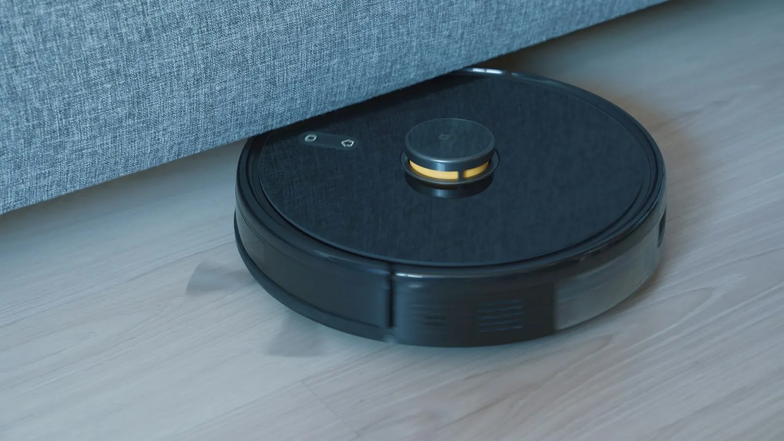 Robot aspirateur noir sur un parquet clair, au pied d'un lit