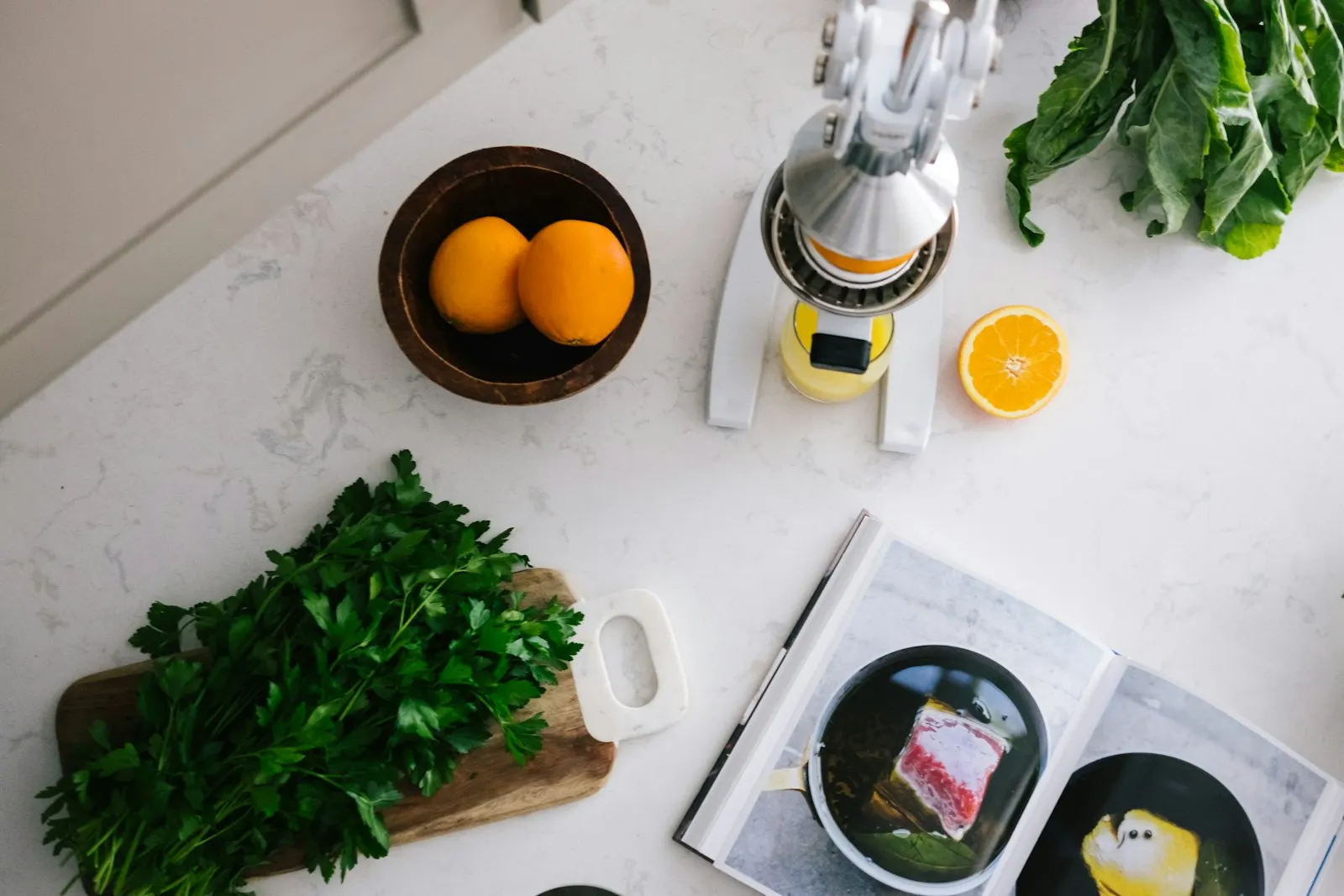 Plan de travail de cuisine avec presse-agrumes, oranges, persil et livre de recettes ouvert