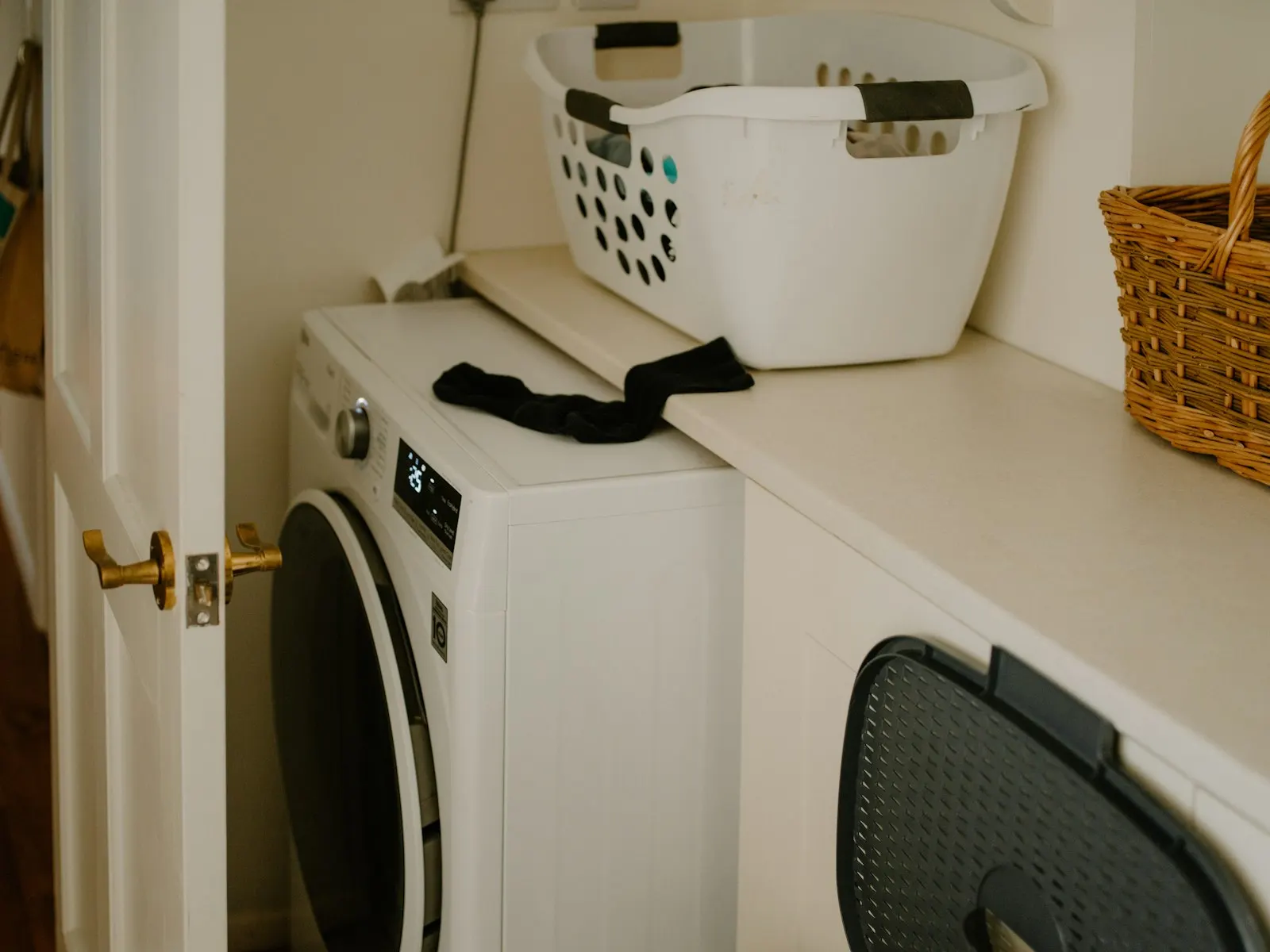 Lave-linge blanc à hublot dans une buanderie, panier à linge posé au-dessus