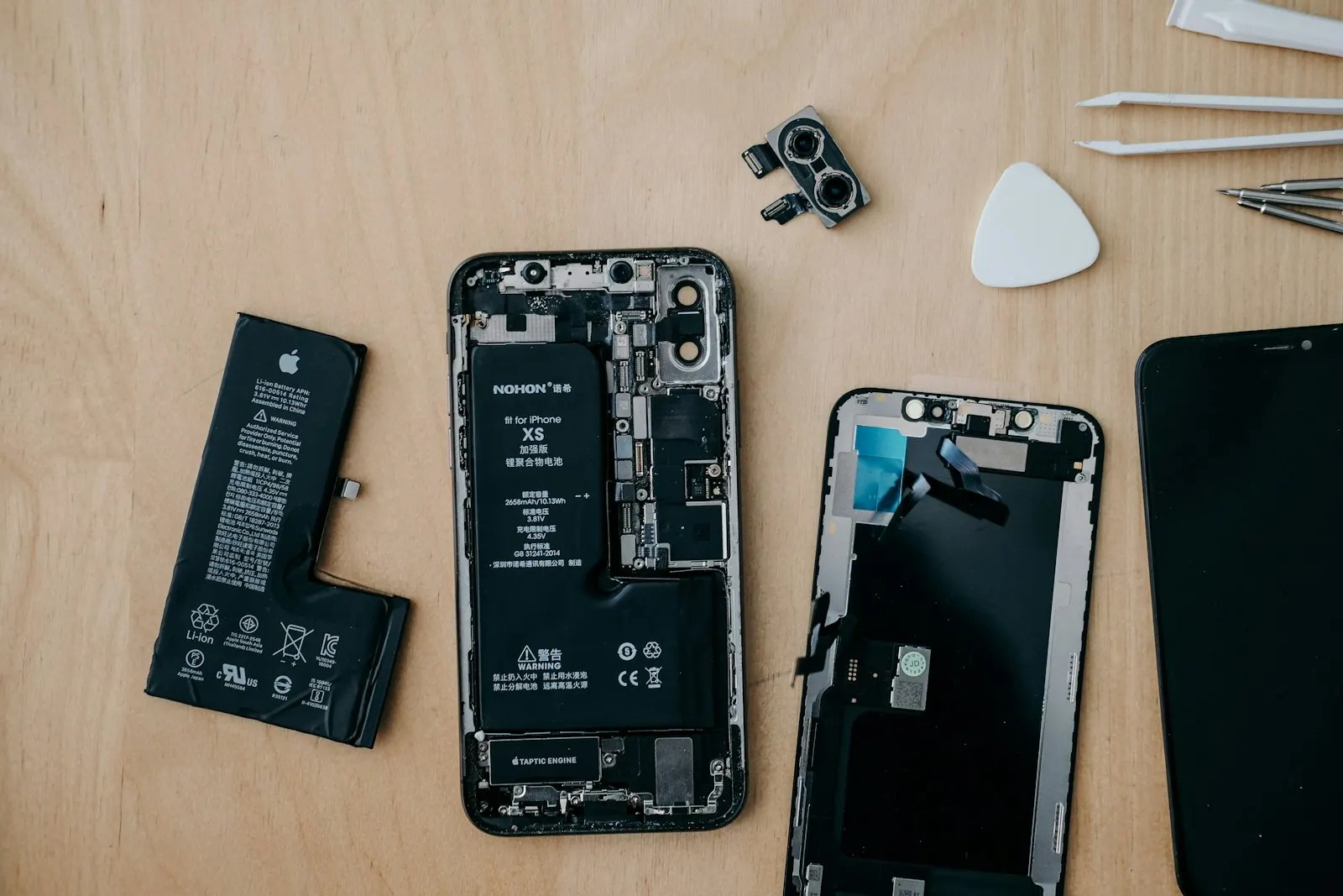 iPhone ouvert en cours de réparation, batterie et écran démontés sur un plan de travail