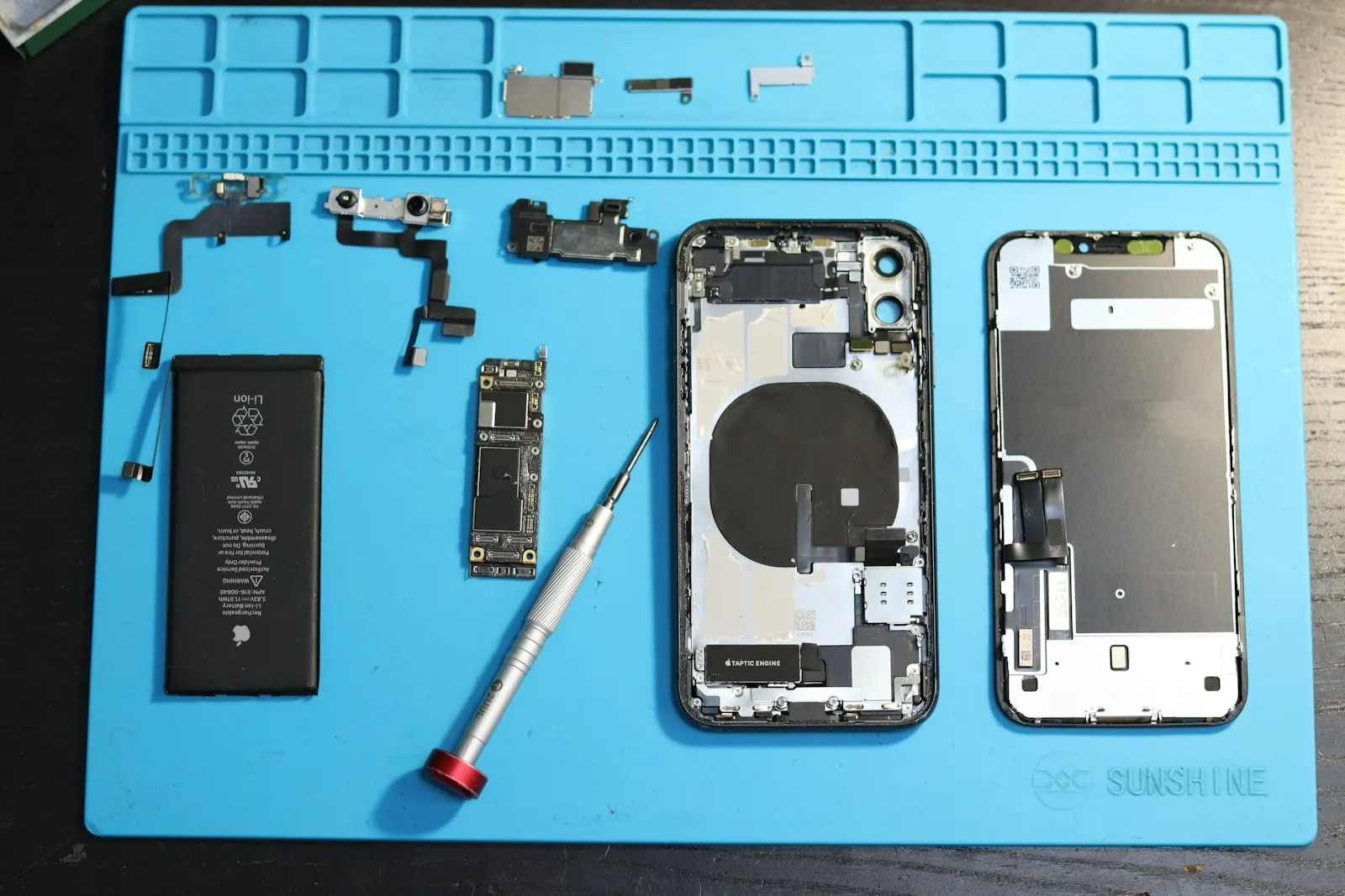 Pièces détachées d'un iPhone démonté, batterie et carte mère, sur un tapis de réparation bleu