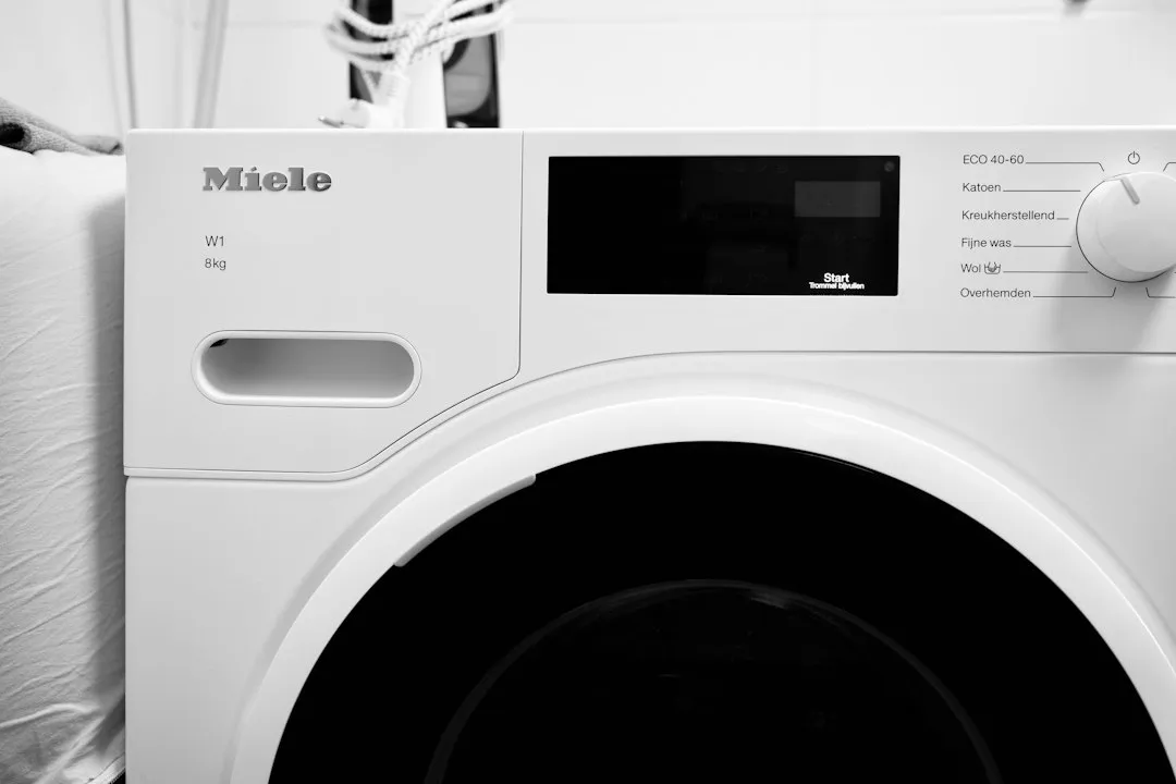 Gros plan sur la façade d'un lave-linge blanc Miele, hublot fermé et bandeau de commandes